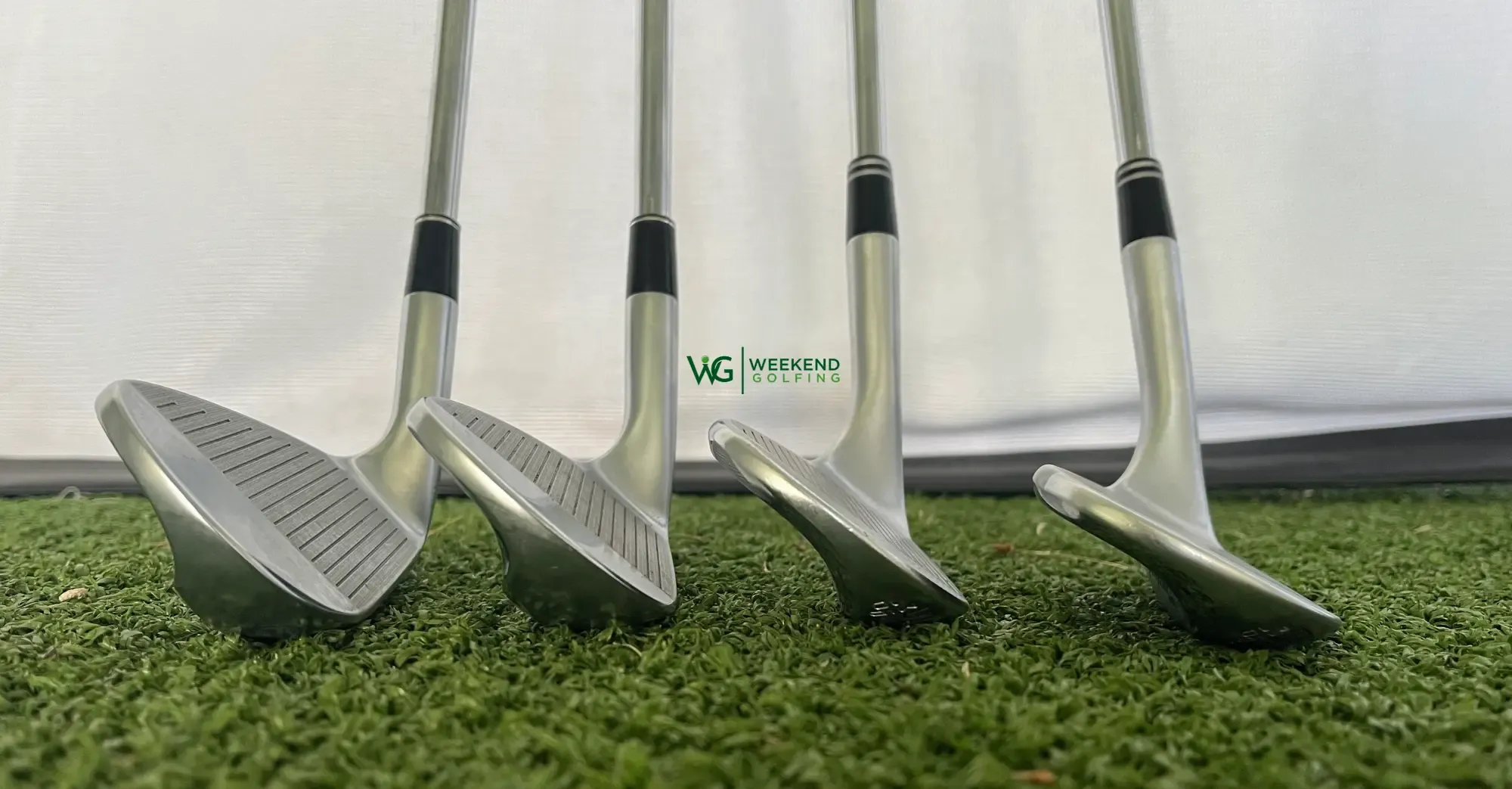 Four golf wedges lined up on turf, sole down, showing how the face angle gets more lofted from left to right.